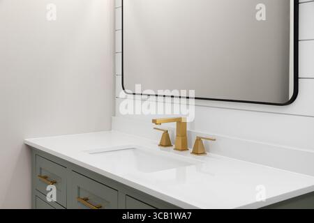 Un lavandino del bagno con un rubinetto dorato su un ripiano in marmo bianco, armadio verde salvia con dettagli in metallo dorato, specchio nero e parete shiplap. Foto Stock