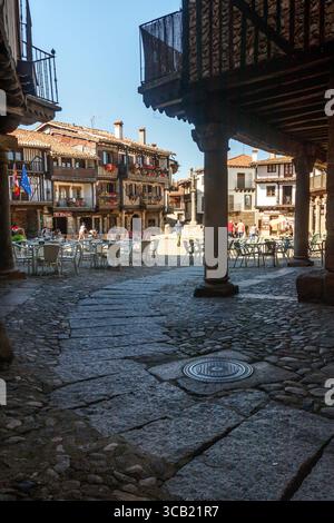 La Alberca, Spagna. 31/5/2024: Strada acciottolata con portici all'ombra, con la Plaza Mayor sullo sfondo illuminata dal sole nella vill Foto Stock
