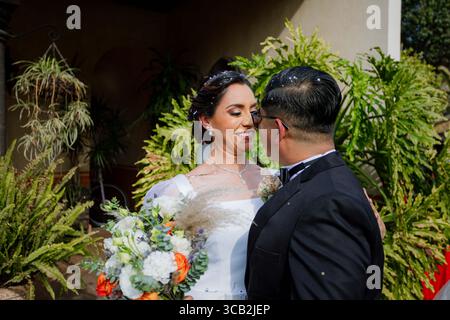 Gli sposi condividono uno sguardo tenero, circondato da una vegetazione lussureggiante, in un primo piano che mette in risalto il loro amore e l'eleganza del matrimonio. Foto Stock