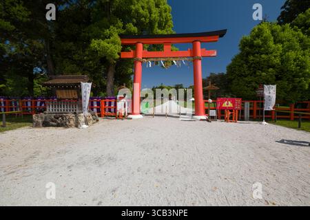 Una vivace porta rossa di Ichi no Torii sorge in un tranquillo parco circondato da vegetazione lussureggiante e sentieri di ghiaia, a simboleggiare l'ingresso di un luogo sacro. Foto Stock