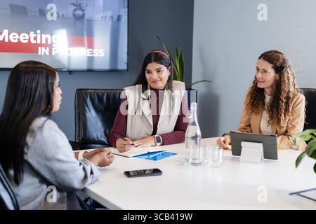 Diverse collaboratrici che indossano blazer che rivedono la presentazione su un tablet nella sala riunioni Foto Stock
