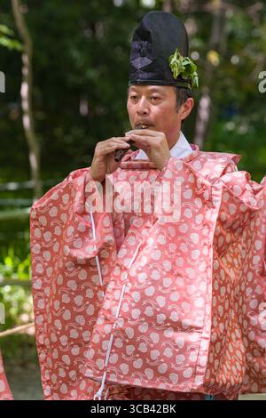 Un musicista giapponese in un tradizionale kimono rosa suona un flauto durante lo Yabusame Shinji. I motivi intricati e l'abbigliamento culturale sottolineano l'im Foto Stock