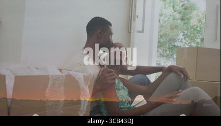 Baciare la coppia che si coccola sul pavimento nell'area soggiorno, con scatole mobili in cartone e avvolgimento a bolle Foto Stock