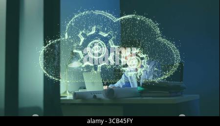 Un professionista IT che indossa una maglietta sul notebook in un ufficio poco illuminato, con ologramma sul cloud e spazio per le copie Foto Stock