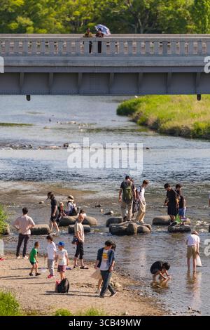 Una vivace scena di famiglie e singoli che si godono una giornata di sole sul fiume Takano, sul delta di Kamogawa, sul Sakyo Ward, Kyoto, Kansai, Honshu, Giappone Foto Stock