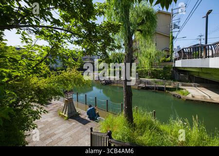 Canale di Jikkokubune con vegetazione che circonda un tranquillo corso d'acqua e un ponte sullo sfondo, Fushimi Ward, Kyoto, Kansai, Honshu, Giappone Foto Stock