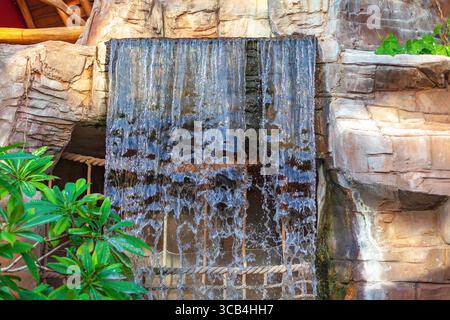 Cascata, incorniciata da formazioni rocciose scolpite, crea una scena tranquilla. L'acqua scorre liberamente lungo un muro di pietra, circondato da vegetazione lussureggiante Foto Stock