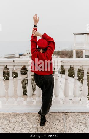 Balcone per donne, maglione rosso e berretto, con vista sull'oceano dalla terrazza. Foto Stock