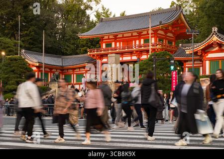 Motion Blur cattura una folla affollata che attraversa la strada vicino alla porta di Yasaka Jinja Nishiromon, circondata dal verde, mostrando l'architettura culturale J. Foto Stock