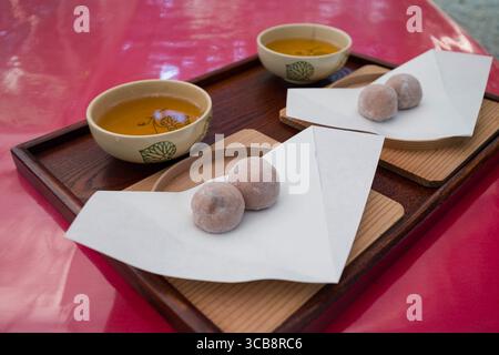 Deliziosi dolci di riso mochi Monkey abbinati a tè fresco servito su tradizionali vassoi di legno, creando un'autentica esperienza culinaria giapponese Foto Stock