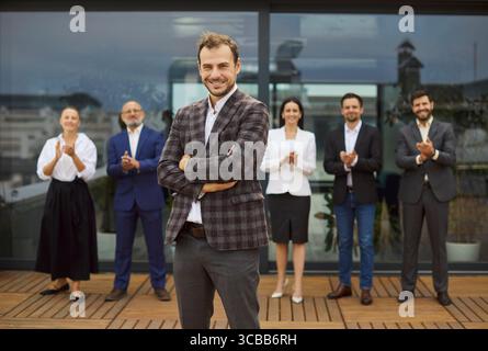 Leader aziendale fiducioso davanti al gruppo di dipendenti applaudito vicino all'edificio degli uffici Foto Stock