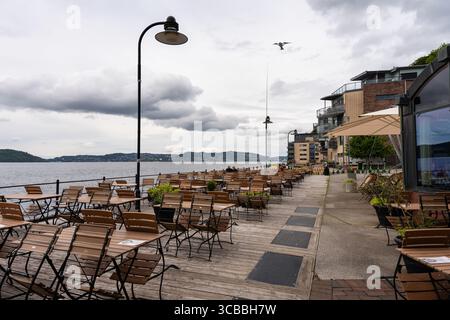 Bergen, Norvegia - 6 luglio 2024: Terrazza con caffè all'aperto con tavoli in legno lungo il lungomare, cielo nuvoloso Foto Stock