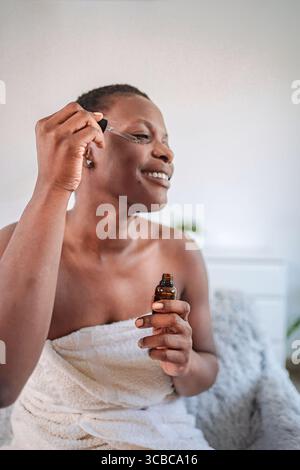 Giovane donna che le applica olio essenziale sul viso Foto Stock