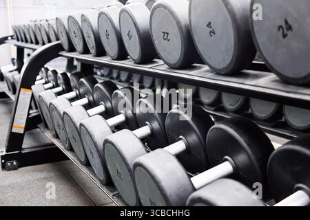 Concetto di sport fitness. Set di manubri neri. Avvicinati a molti manubri in metallo sul rack nel centro fitness sportivo Foto Stock