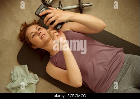 Fitness in casa, donna che usa il suo smartphone per l'allenamento Foto Stock