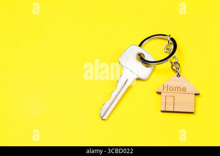 Portachiavi a forma di casa in legno e chiave su sfondo giallo. Spazio libero. Foto Stock