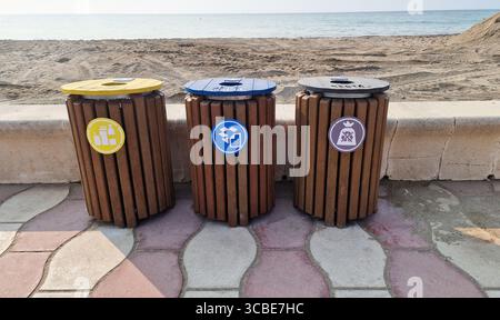 Almeria, Spagna - 25 maggio 2025: Tre distinti contenitori in legno sono posizionati sulla spiaggia sabbiosa, incoraggiando il riciclaggio e la responsabilità ambientale Foto Stock