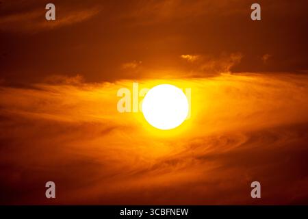 Un incredibile teleobiettivo in primo piano del sole che tramonta, che brilla di calore intenso in un bellissimo cielo arancione. Foto Stock