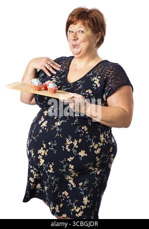 Cinquanta qualcosa di donna che tiene in mano un piatto di piccolo cupcake colorato dall'espressione simpatica Foto Stock