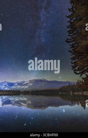 16 ottobre 2022, Alberta, Canada: Le costellazioni autunnali di Perseo e Cassiopea, con la luminosa Capella ad Auriga e l'ammasso stellare delle Pleiadi in Toro, sul fondo, che si innalza a nord-est sul Lago Edith nel Parco Nazionale di Jasper, in una notte d'autunno limpida. Il doppio ammasso si trova al centro, sopra il più grande gruppo di stelle intorno a Mirfak chiamato Associazione Perseus... si tratta di una miscela di un'esposizione singola tracciata di 2 minuti per il cielo e l'acqua con le stelle riflesse, con una pila di due esposizioni di 3 minuti non tracciate per il resto del terreno, entrambe a f/2,8 con l'obiettivo Canon RF15-35mm Foto Stock