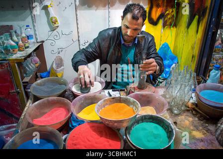 Un venditore ambulante ad Amman, in Giordania, produce bottiglie colorate riempite di sabbia per i turisti. Foto Stock
