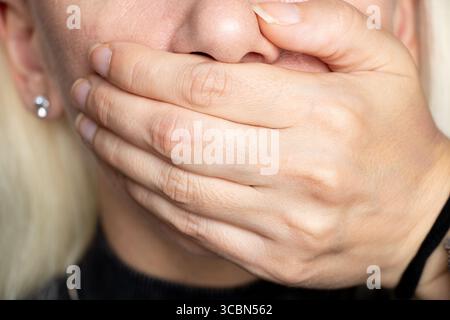 Primo piano della mano di una donna che si copre la bocca come un gesto di silenzio, nasconde un segreto, proibisce la conversazione Foto Stock