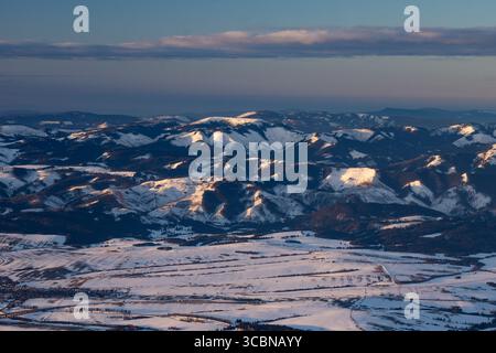 Vista aerea delle cime innevate baciate dal caldo bagliore del sole che tramonta, creando un paesaggio invernale mozzafiato, Liptovský Mikuláš, regione di Žilina, Slovacchia. Foto Stock