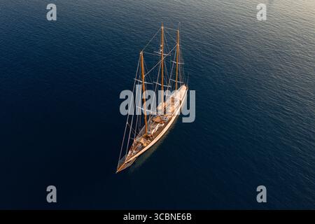 La vista aerea di un maestoso yacht a vela scivola attraverso il blu profondo del Mar Egeo, le sue vele si sono spostate, gettando una lunga ombra sull'acqua, Ermioni, Argolis, Grecia. Foto Stock