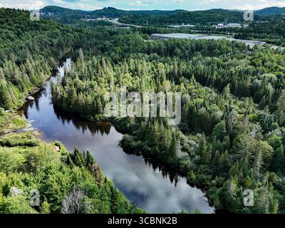 Vista aerea del fiume tortuoso che riflette il cielo, abbracciato da foreste verdeggianti e colline lontane, Saint-Adolphe-d'Howard, Quebec, Canada. Foto Stock