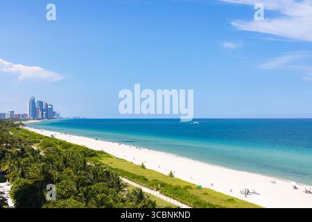 Vista aerea delle acque turchesi dell'Oceano Atlantico che incontrano spiagge di sabbia bianca incontaminate, con lo skyline di Sunny Isles che brilla in lontananza, Surfside, Florida, Stati Uniti. Foto Stock