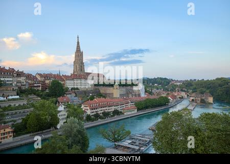Uno splendido panorama di Berna presenta la sua guglia iconica e gli edifici storici lungo il fiume Aare. Le colline verdi sorgono sullo sfondo, creando una pict Foto Stock