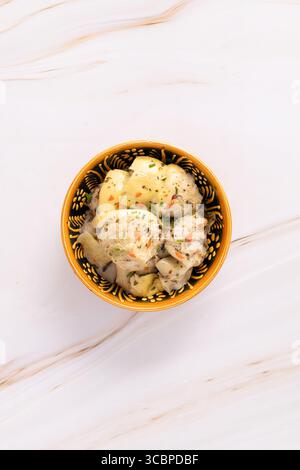 Ciotola di cuori di carciofo marinati con erbe e spezie, servita in un piatto a motivi geometrici su una superficie di marmo. Prodotto M&S, fotografato dall'alto. Foto Stock