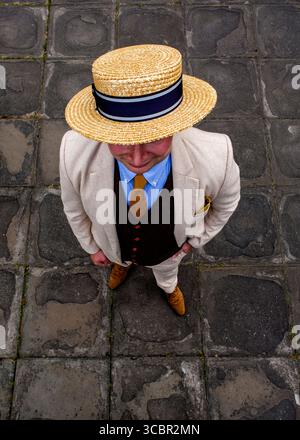 Un uomo con un cappello di paglia, un vestito e una cravatta si trova su una superficie di pietra. Foto Stock