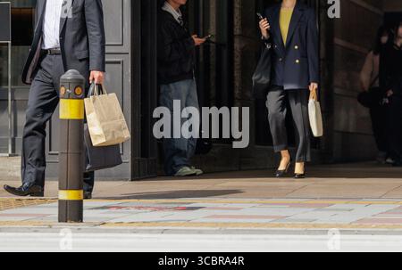 In uscita dal corridoio scuro, uomo d'affari ben vestito con valigetta e teste per sacchetti di carta per una passeggiata urbana seguita da una donna d'affari con smartphone in mano. Foto Stock