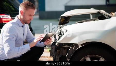 Agente assicurativo che ispeziona White Car dopo un incidente utilizzando il computer tablet. Foto Stock
