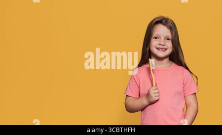Una ragazza felice tiene uno spazzolino tra le mani. Uno scatto panoramico isolato. Un posto per il testo. Odontoiatria pediatrica Foto Stock