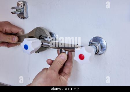 Tenendo il corpo del rubinetto in posizione, mentre la chiave regolabile fissa il dado di montaggio creando un giunto idraulico affidabile sul lavello da cucina in acciaio inox. Foto Stock
