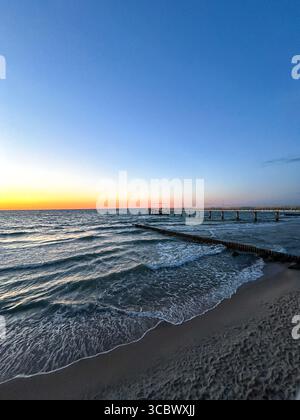 Tramonto dorato sul mare calmo con molo di legno che si estende fino all'acqua. Contenuto di meditazione, estetica soffocante. Foto Stock