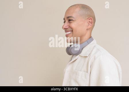Ritratto di un uomo ispanico calvo che indossa una camicia beige casual e cuffie intorno al collo, appoggiato su un semplice sfondo beige. Foto Stock