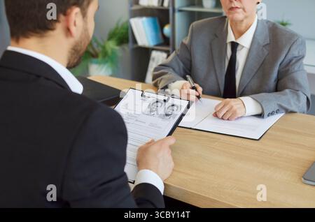 Uomo in cerca di lavoro seduto alla scrivania con cv che parla con un manager HR maturo in carica Foto Stock