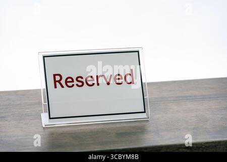 Un cartello riservato con testo in grassetto rosso è posto su un tavolo di legno, che indica che lo spazio è riservato a uno scopo specifico o a una persona. il segno è semplice Foto Stock
