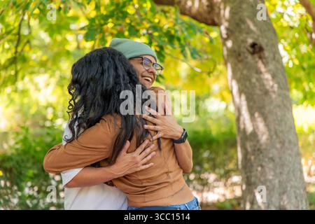 Due gioiosi amici multietnici che si abbracciano in un parco, condividendo un momento di affetto e di connessione sentiti mentre sono circondati dalla bellezza Foto Stock