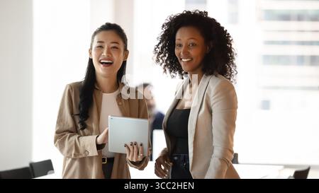 Felice sorridere diverse giovani donne compagne di squadra in piedi insieme a un tablet Foto Stock