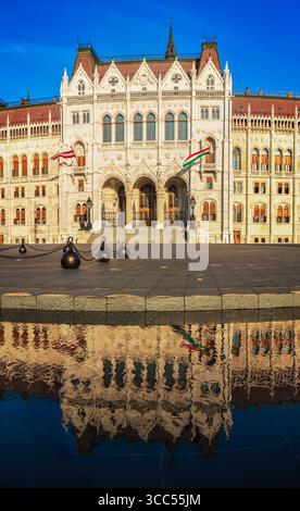 Edificio del Parlamento ungherese a Budapest, riflesso nell'acqua, splendida architettura neogotica con bandiere Foto Stock