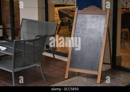 Area con posti a sedere all'aperto con menu di lavagna vicino al caffè Foto Stock