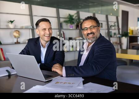 Giovani e vecchi partner commerciali felici che lavorano al notebook Foto Stock