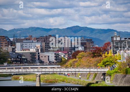 Splendida città di Kyoto caratterizzata da un ponte su un fiume tranquillo, circondato da edifici moderni e da un vivace fogliame autunnale, con montagne maestose Foto Stock