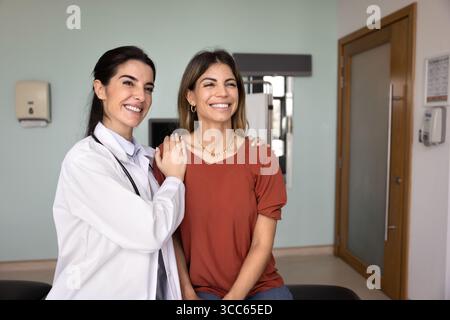 Allegro giovane medico latino che tocca le spalle di una paziente Foto Stock