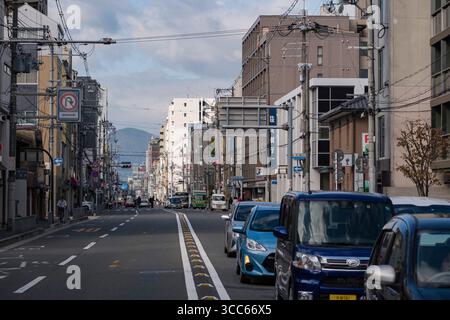 Guardando verso est lungo Marutamachi Dori, traffico intenso e cielo limpido. L'immagine cattura la vita urbana quotidiana e l'architettura moderna, con veicoli e peo Foto Stock