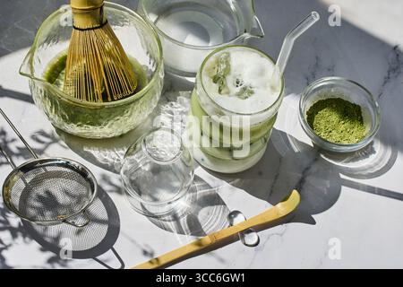 Aggiornamento dell'impostazione Matcha. Una disposizione illuminata dal sole di utensili da tè matcha con un latte matcha freddo spalmabile. Foto Stock
